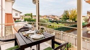 Un balcón con mesa lista para comer, sillas y vista a una zona residencial.