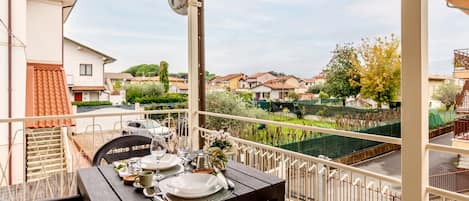 A balcony with a table set for dining, chairs, and a view of a residential area.