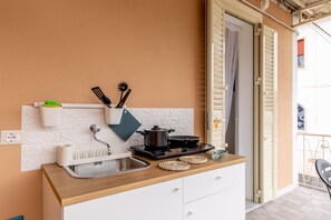 Een kleine keuken met een spoelbak, kookplaat en witte keukenkastjes.