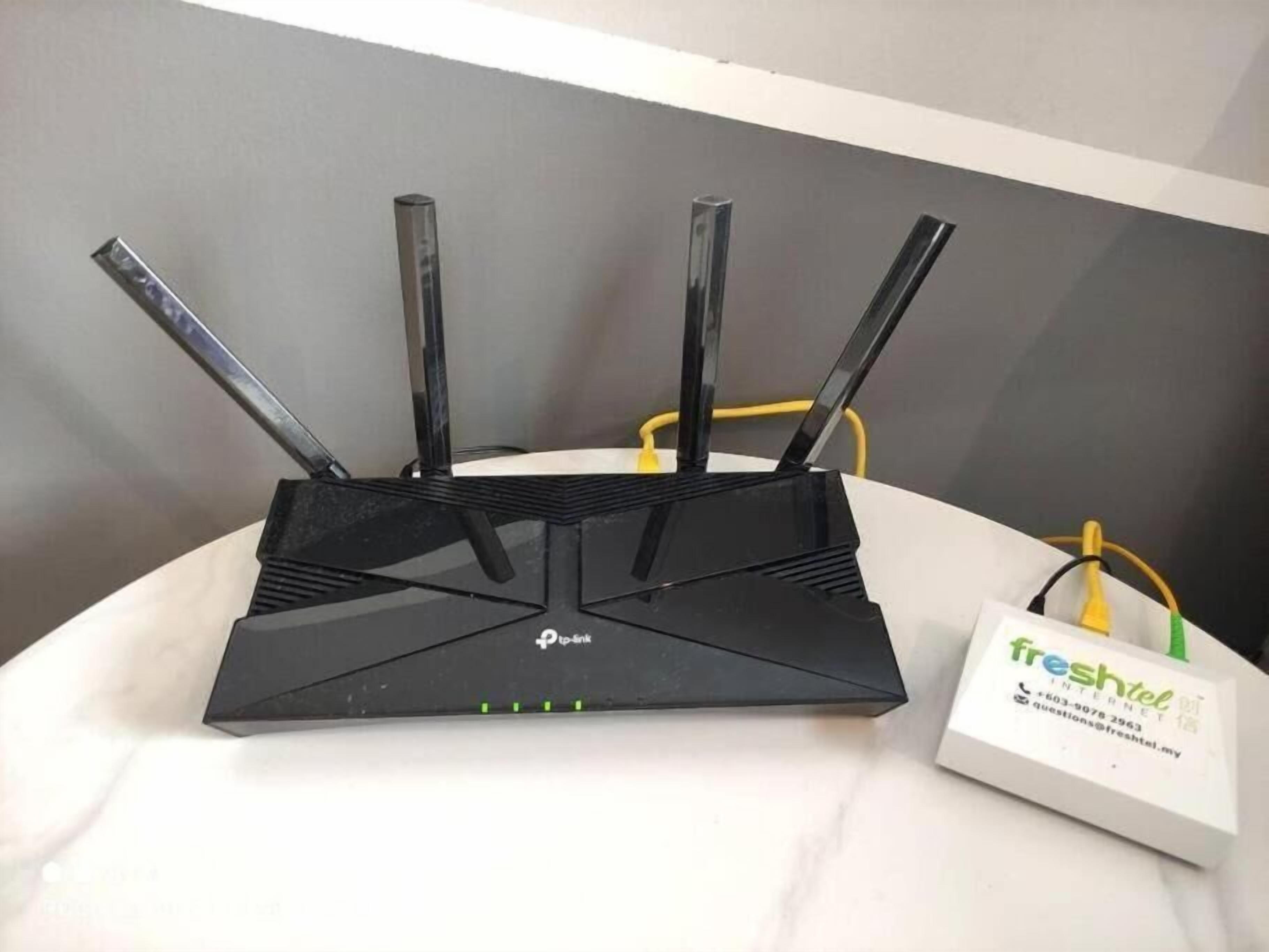 Un router TP-Link negro con cuatro antenas sobre una superficie de mármol blanco, junto a una caja de Internet FreshTel blanca.