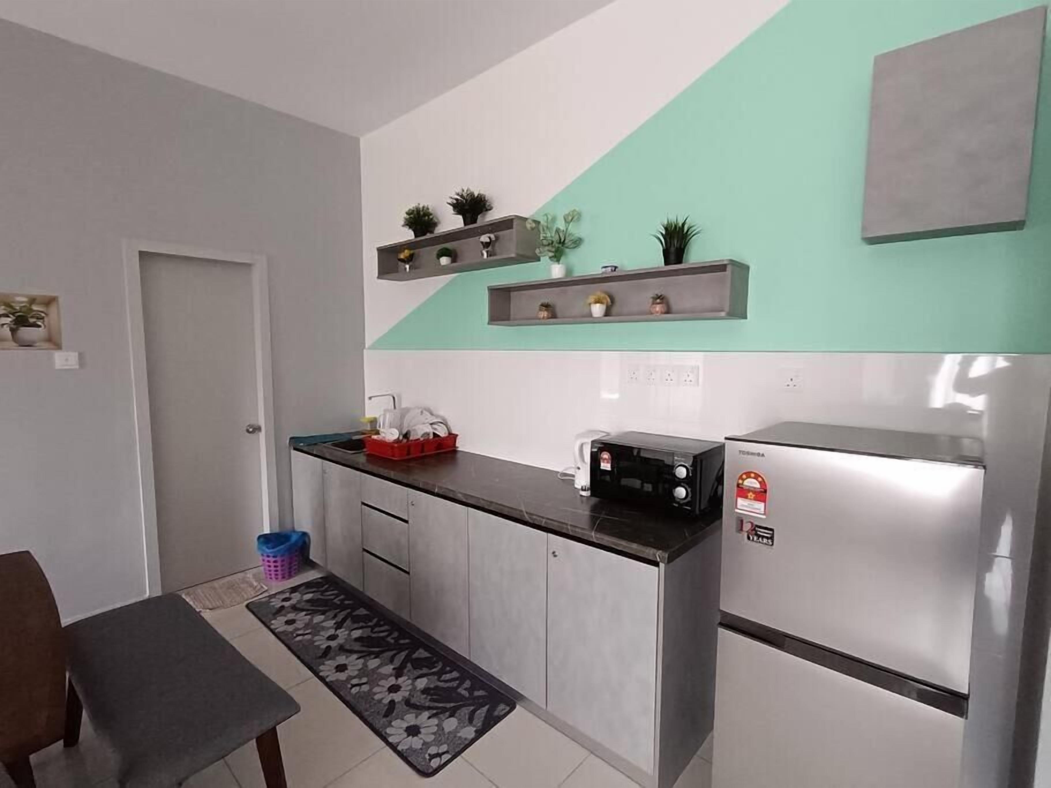 A compact kitchen with a refrigerator, microwave, and a small countertop. There are shelves above the counter holding decorative items and plants.