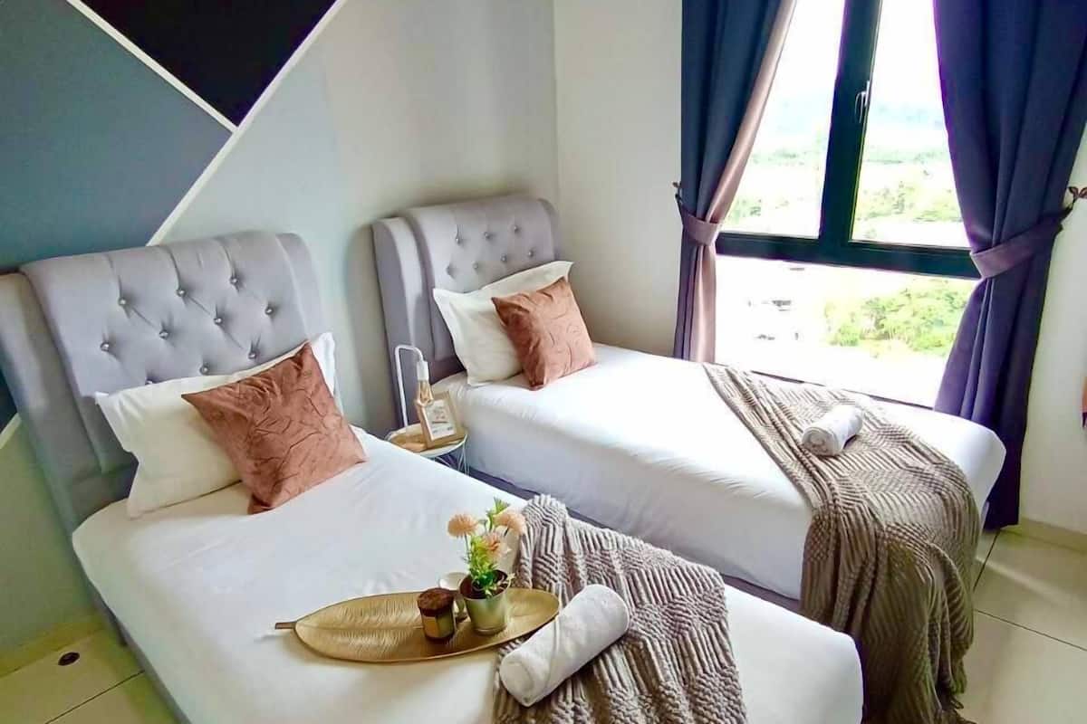 A modern hotel room with two beds, each with a tufted headboard, white bedding, and decorative pillows. A tray with flowers and a candle is on the bed.