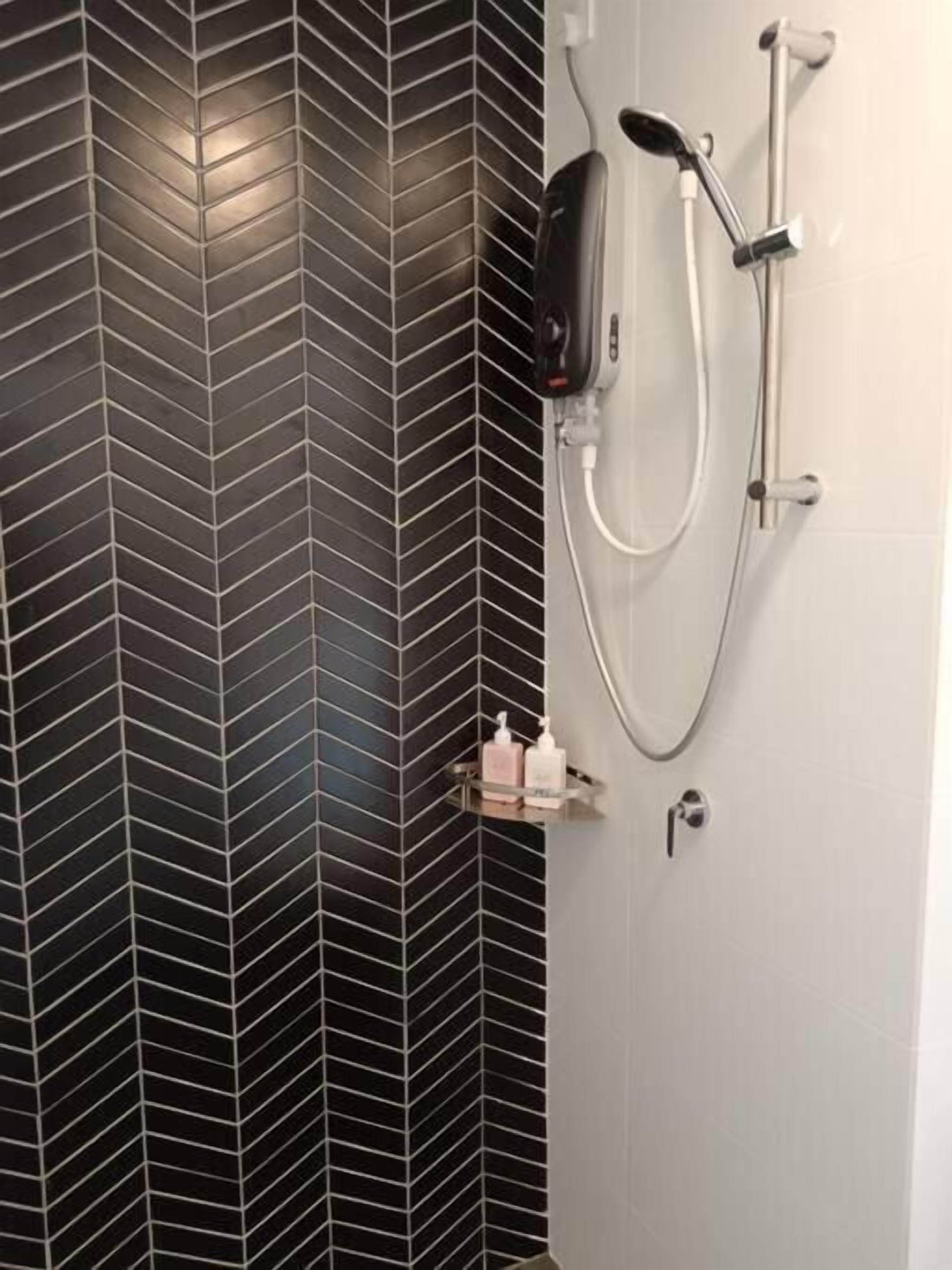 A bathroom with a black and white herringbone tile wall, a shower with a handheld showerhead, and a small shelf with toiletries.