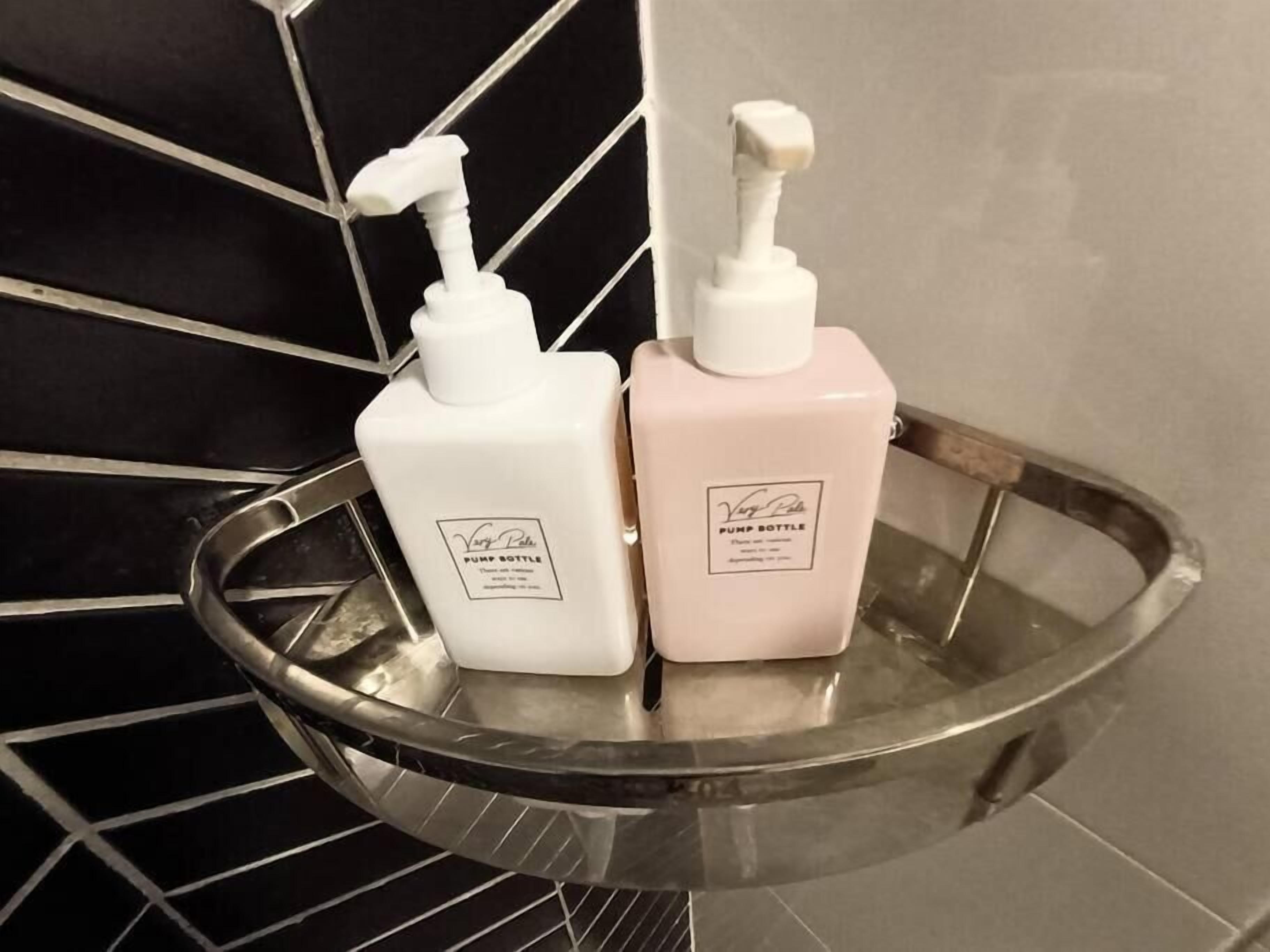 Two pump bottles on a metallic tray in a bathroom with black and beige tiles.