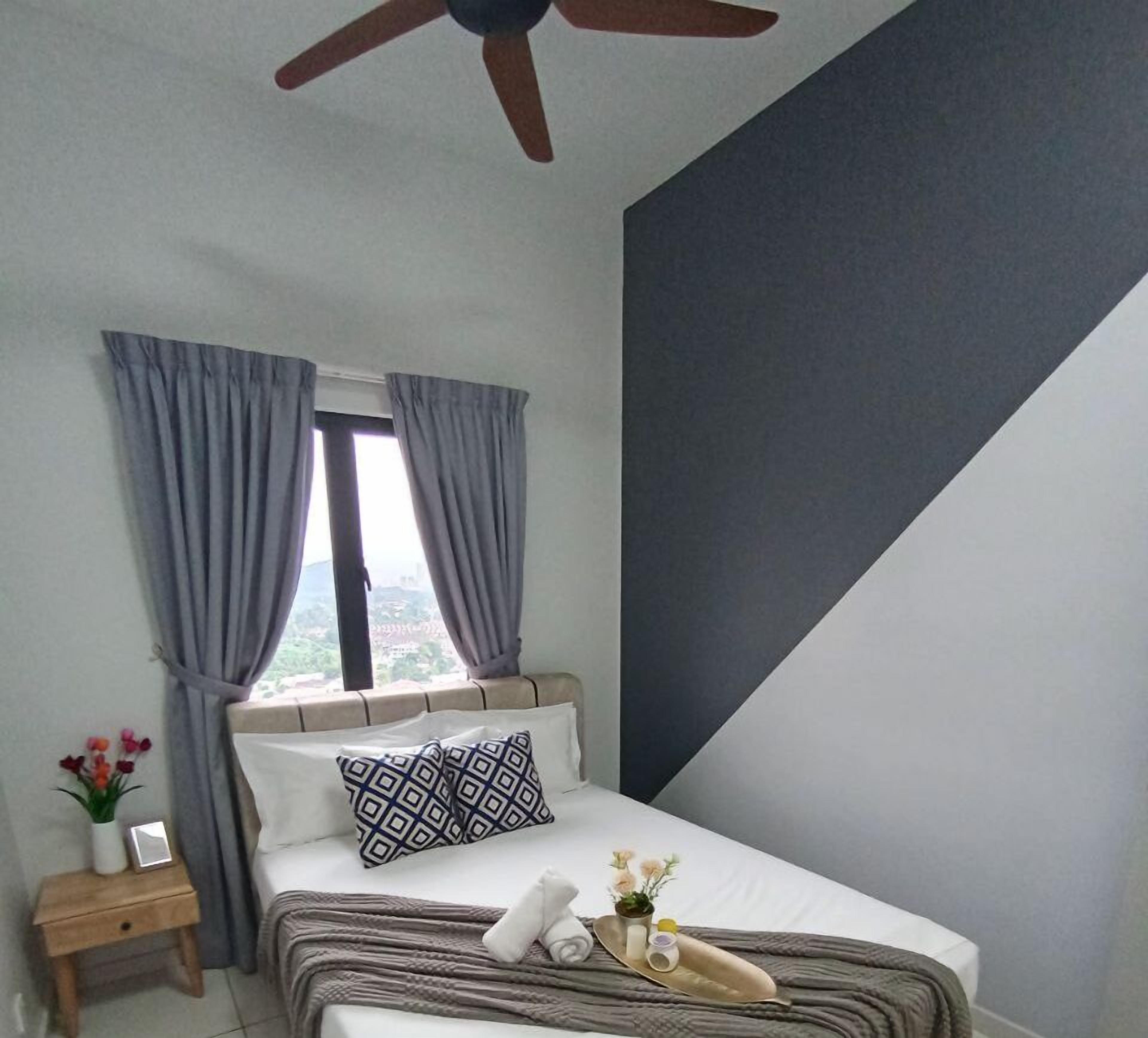 A bedroom with a bed, a nightstand, a window with curtains, a ceiling fan, and a view of the outside.