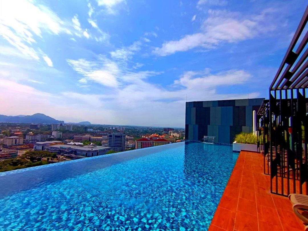 Una piscina infinita en la azotea con vistas a la ciudad, un edificio moderno y un cielo despejado.