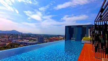 Una piscina infinita en la azotea con vistas a la ciudad, un edificio moderno y un cielo despejado.