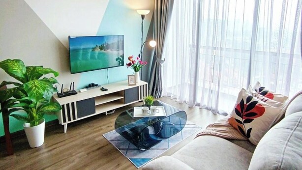 Una sala moderna con una televisión de pantalla plana, un ventilador de techo, un sofá, una mesa de centro y un amplio ventanal con cortinas.