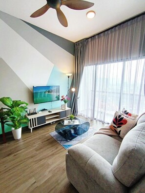 Una sala moderna con una televisión de pantalla plana, un ventilador de techo, un sofá, una mesa de centro y un amplio ventanal con cortinas.