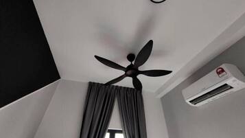 Un ventilador de techo, una ventana con cortinas y un equipo de aire acondicionado en una habitación.