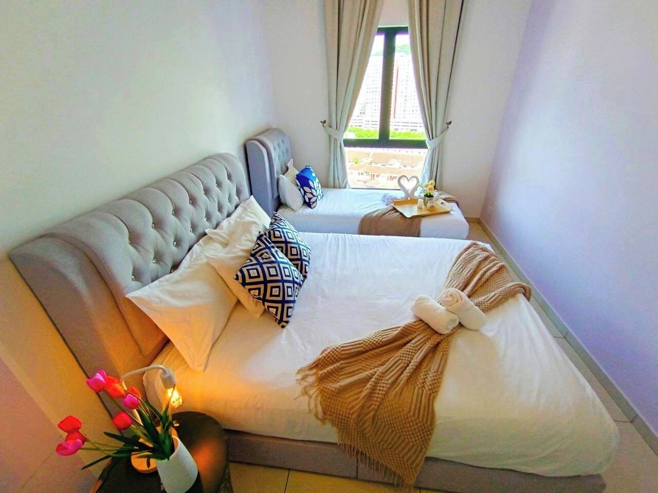 A neatly made bed with a tufted headboard, white bedding, and decorative pillows. A woven throw blanket is draped over the foot of the bed.