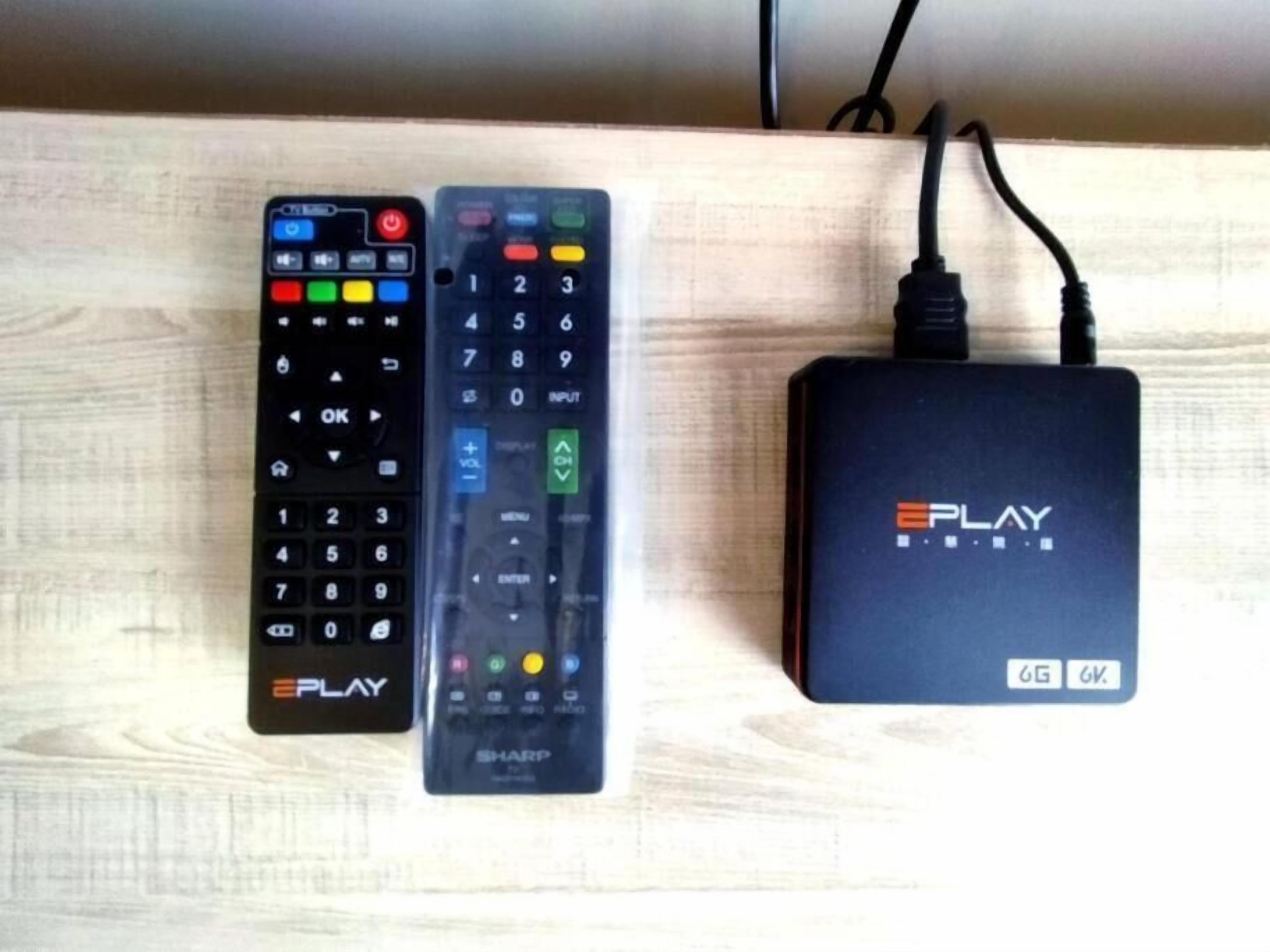 Three remote controls and a black electronic device on a wooden surface.