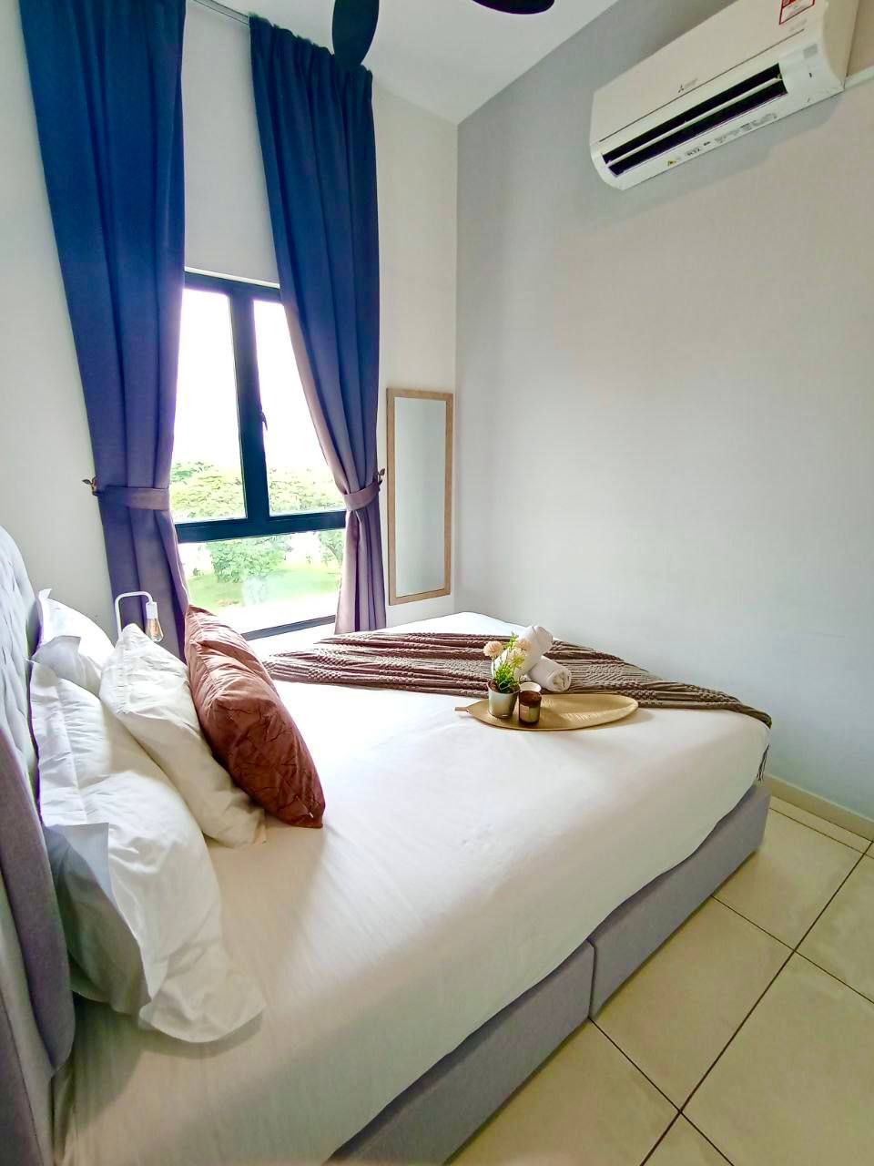 A neatly made bed with pillows, a bedside table with a vase, and a window with curtains.