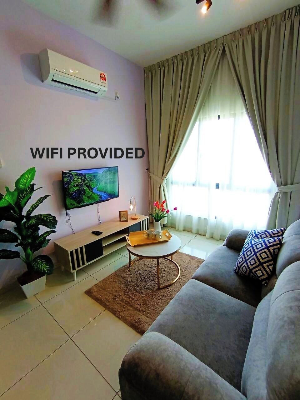 A living room with a sofa, a coffee table, a TV, and a sign stating "WIFI PROVIDED".