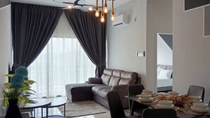 Una sala de estar moderna con un sofá, una mesa de comedor y sillas. Hay una planta y una ventana con cortinas.