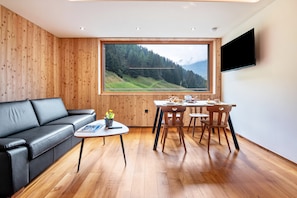 Un salon moderne avec un mur en bois, un canapé en cuir noir, une table à manger avec des chaises et une grande fenêtre donnant sur les montagnes.