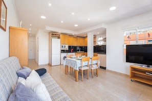 A modern living room with a sofa, dining table, chairs, and a TV.