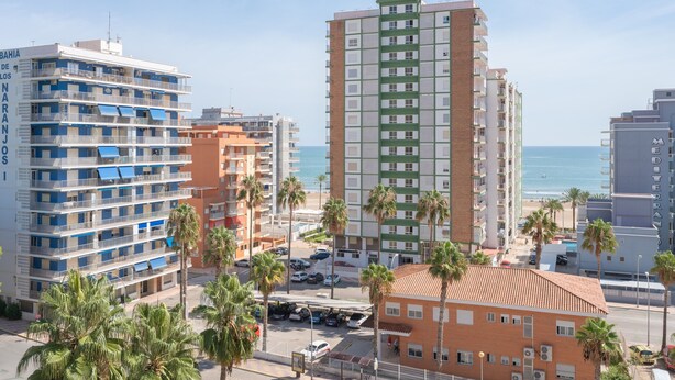 A coastal cityscape with multi-story buildings, palm trees, and a clear view of the sea.