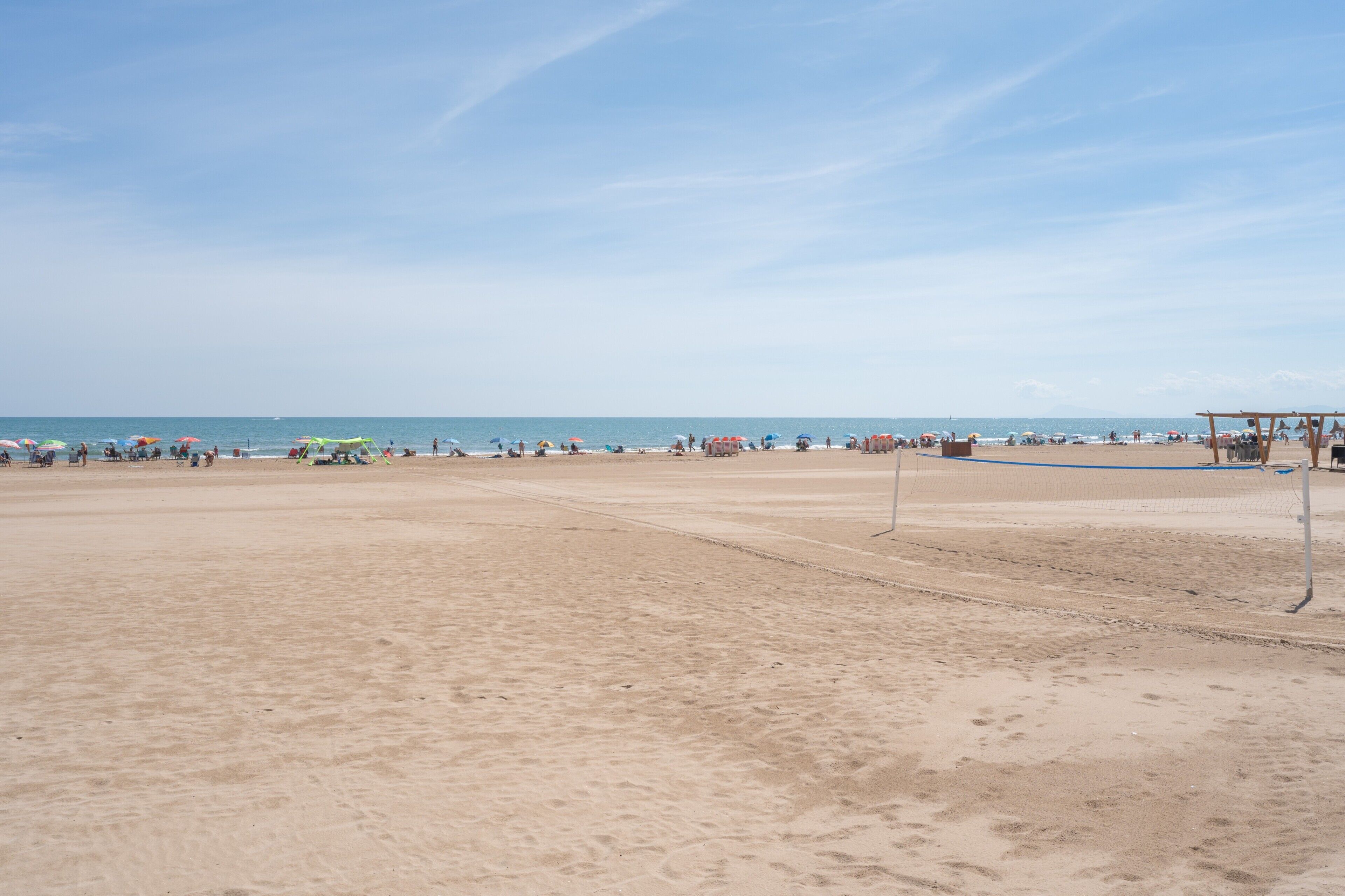Una playa con una red de voleibol, sombrillas y gente.