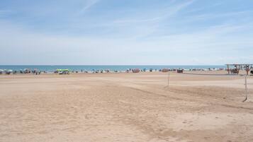 Una playa con una red de voleibol, sombrillas y gente.