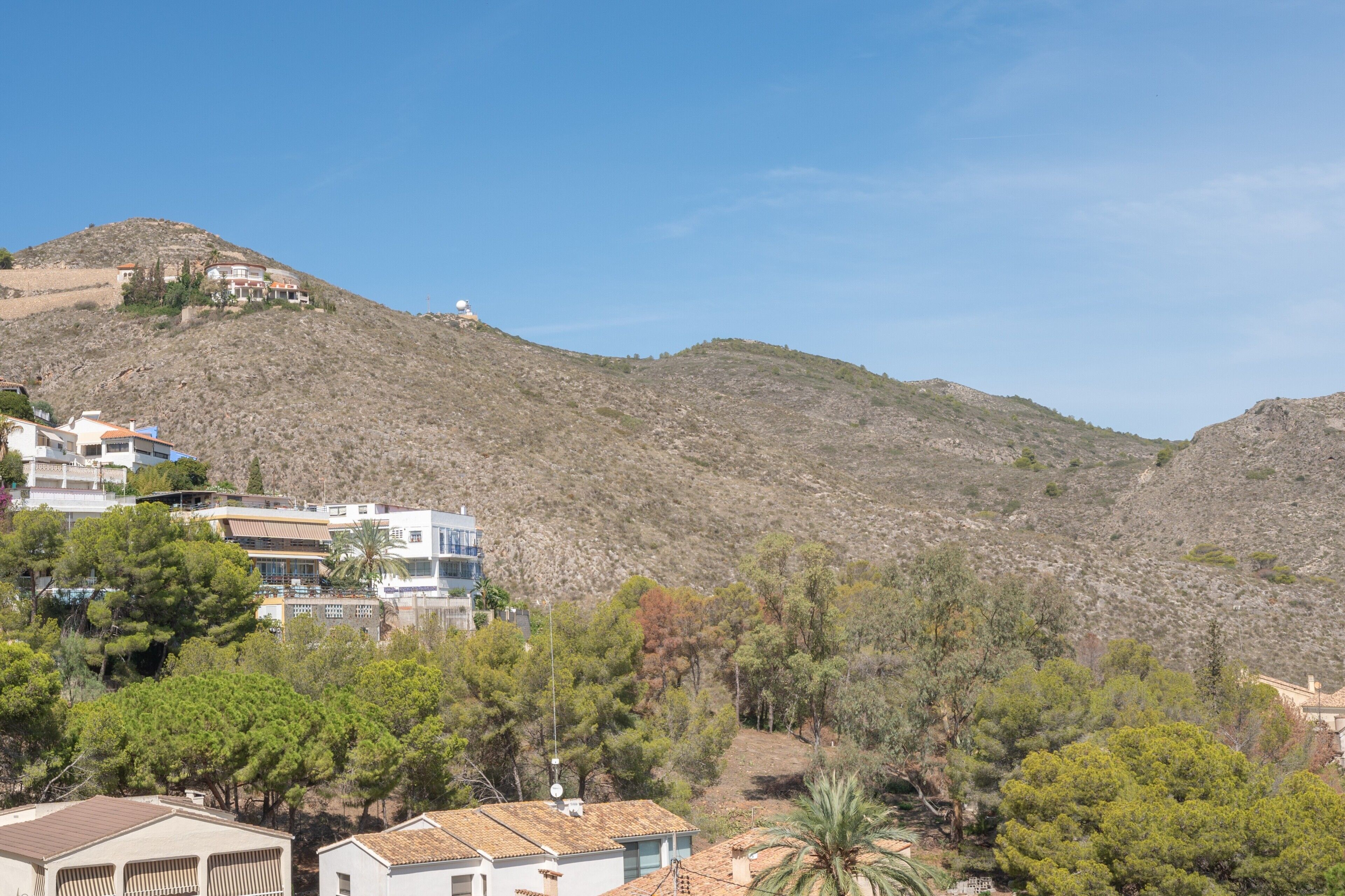 A hillside residential area with houses, some with visible satellite dishes, and a clear sky.