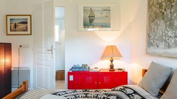 A bedroom with a bed, a red dresser, a lamp, and a painting on the wall.