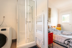 Een slaapkamer met een bed, een rode dressoir, een glazen douchecabine en een raam.