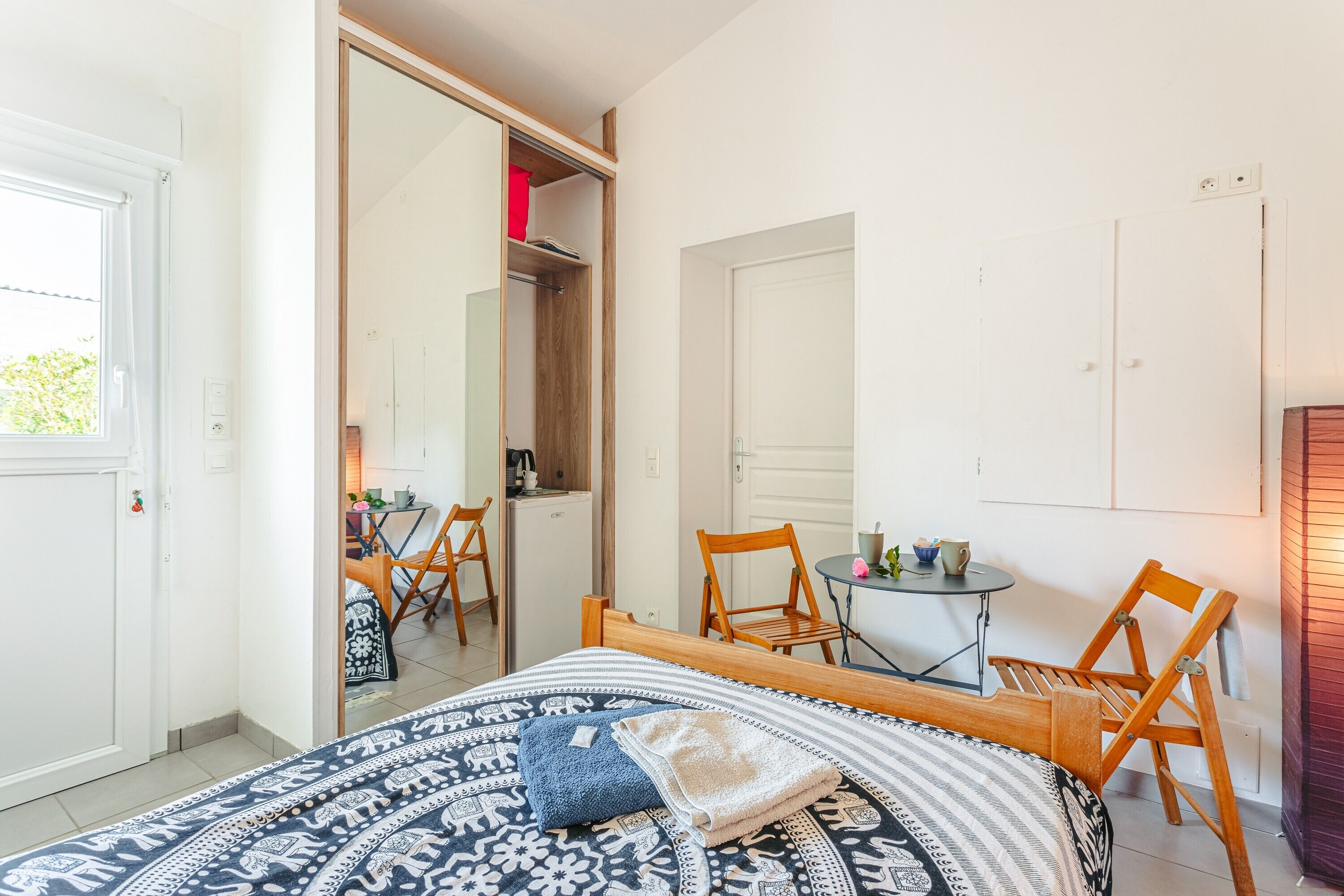 A bedroom with a bed, two wooden chairs, a small table, and a mirror.