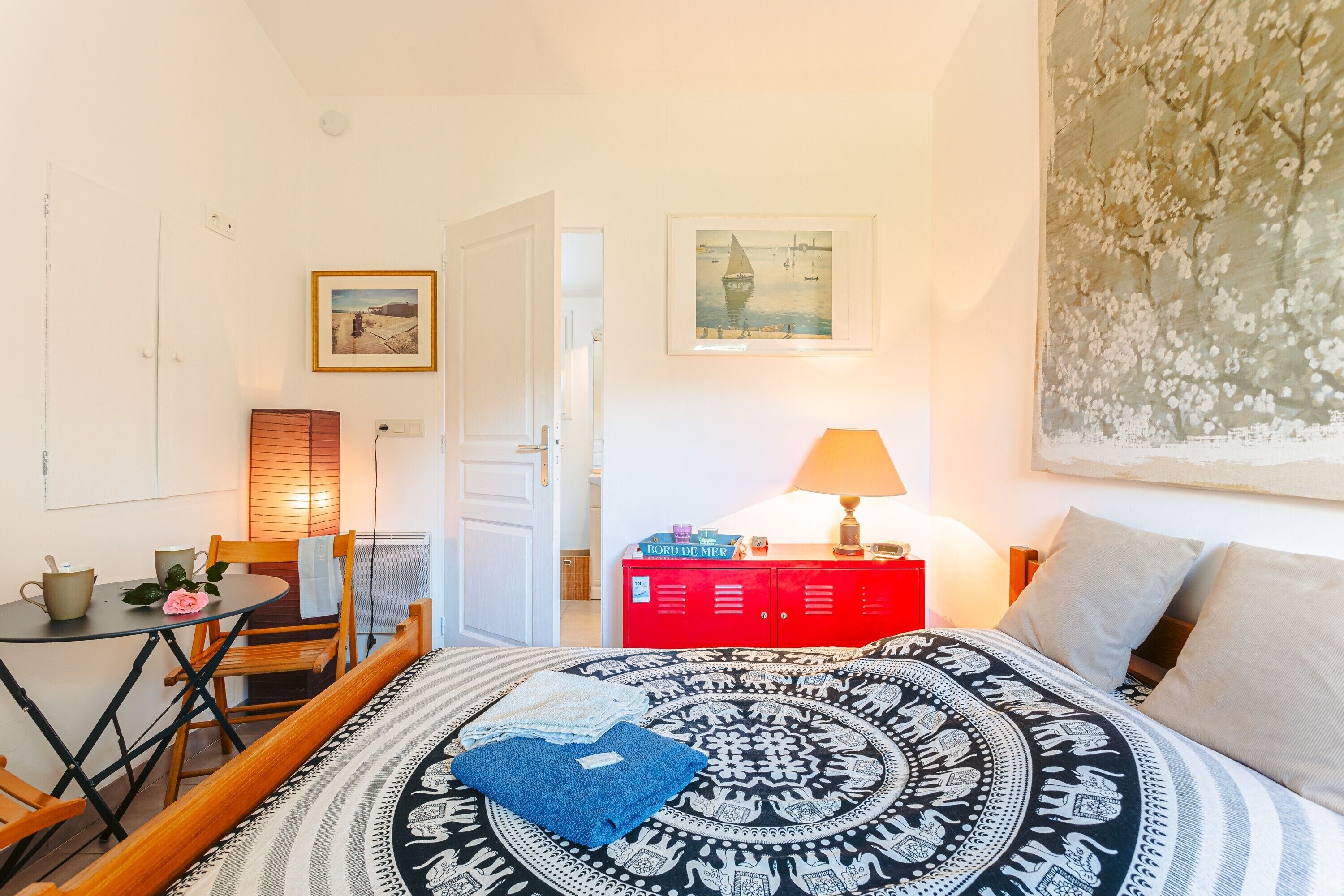 Una habitación con cama, una mesa con sillas, un armario rojo y un cuadro en la pared.