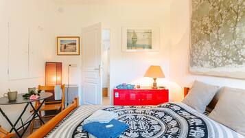 Una habitación con cama, una mesa con sillas, un armario rojo y un cuadro en la pared.