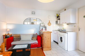 A compact living space with a sofa, a small table, a washing machine, and a kitchenette.