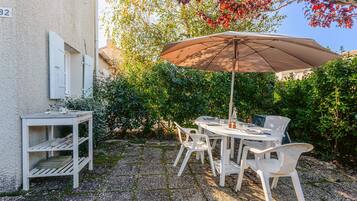 Un patio con una mesa, sillas, una sombrilla y un estante blanco pequeño.