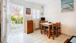 Een keuken met een eettafel, stoelen, een televisie en een raam met uitzicht op een tuin.