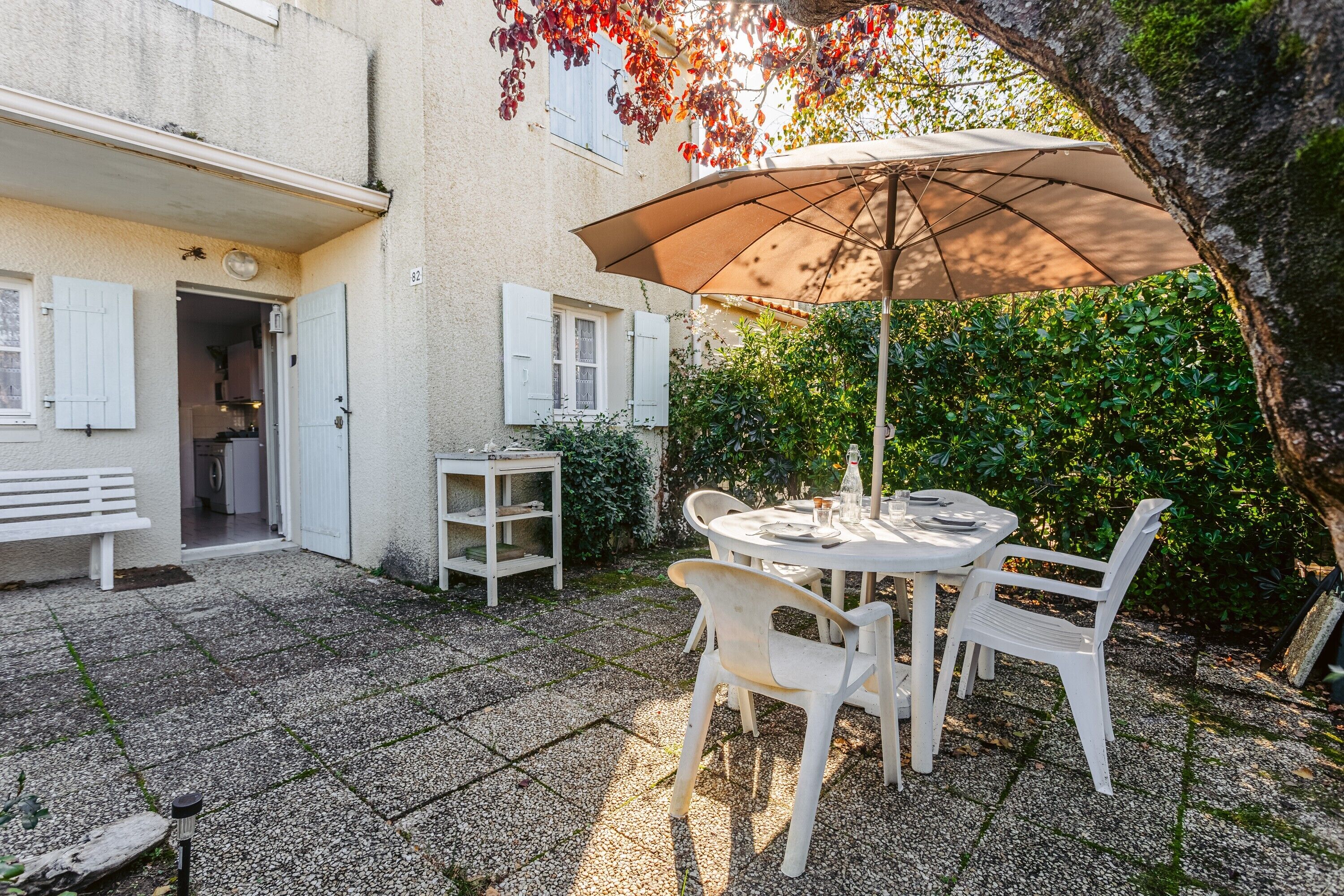 Un patio exterior con una mesa, sillas, un banco y un paraguas grande.