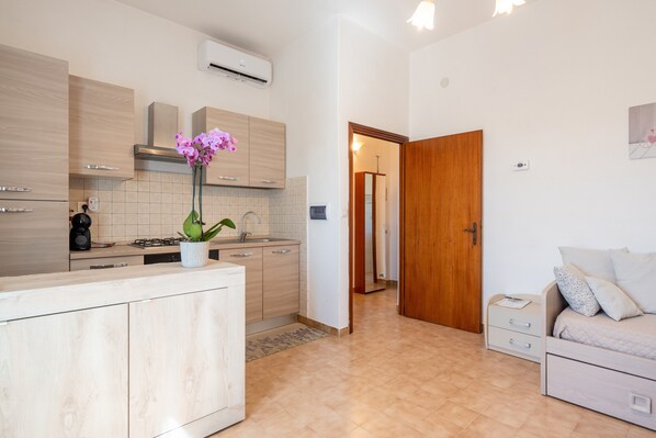 A modern kitchen with a central island, a dining area with a sofa, and a wooden door leading to another room.