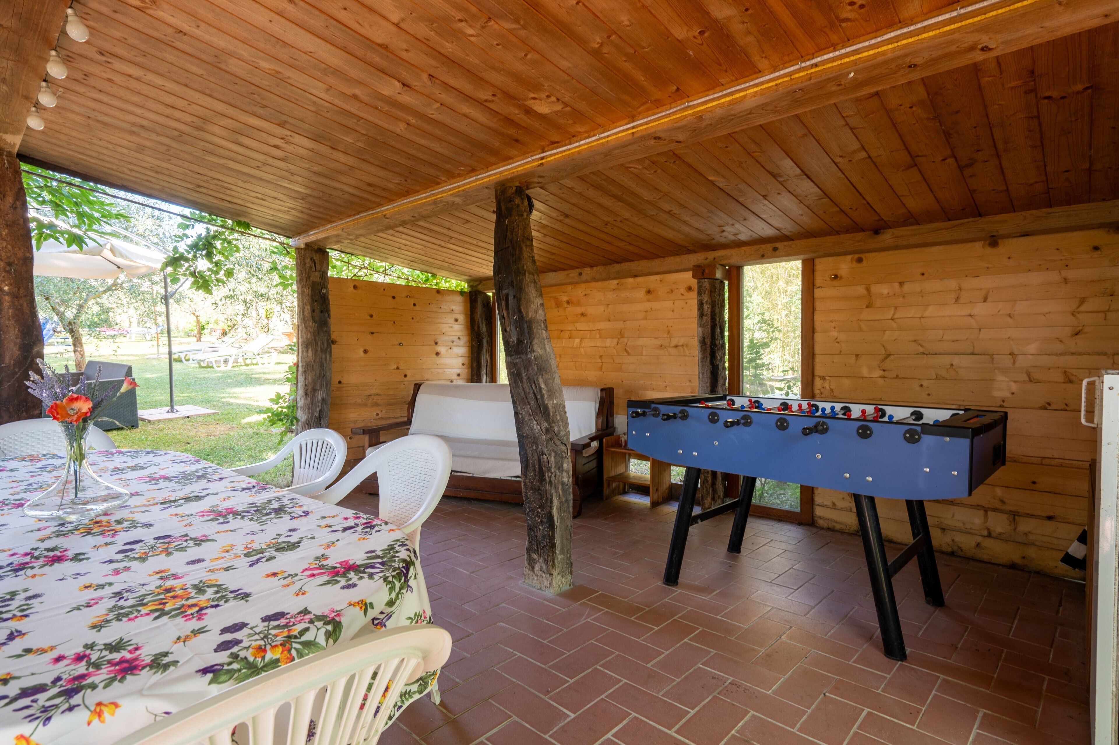 Une pièce au plancher de bois, avec un baby-foot, une table recouverte d’une nappe à motifs floraux et une chaise blanche.
