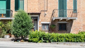 Un bâtiment en briques avec des volets verts, un petit balcon et un arbre au premier plan.