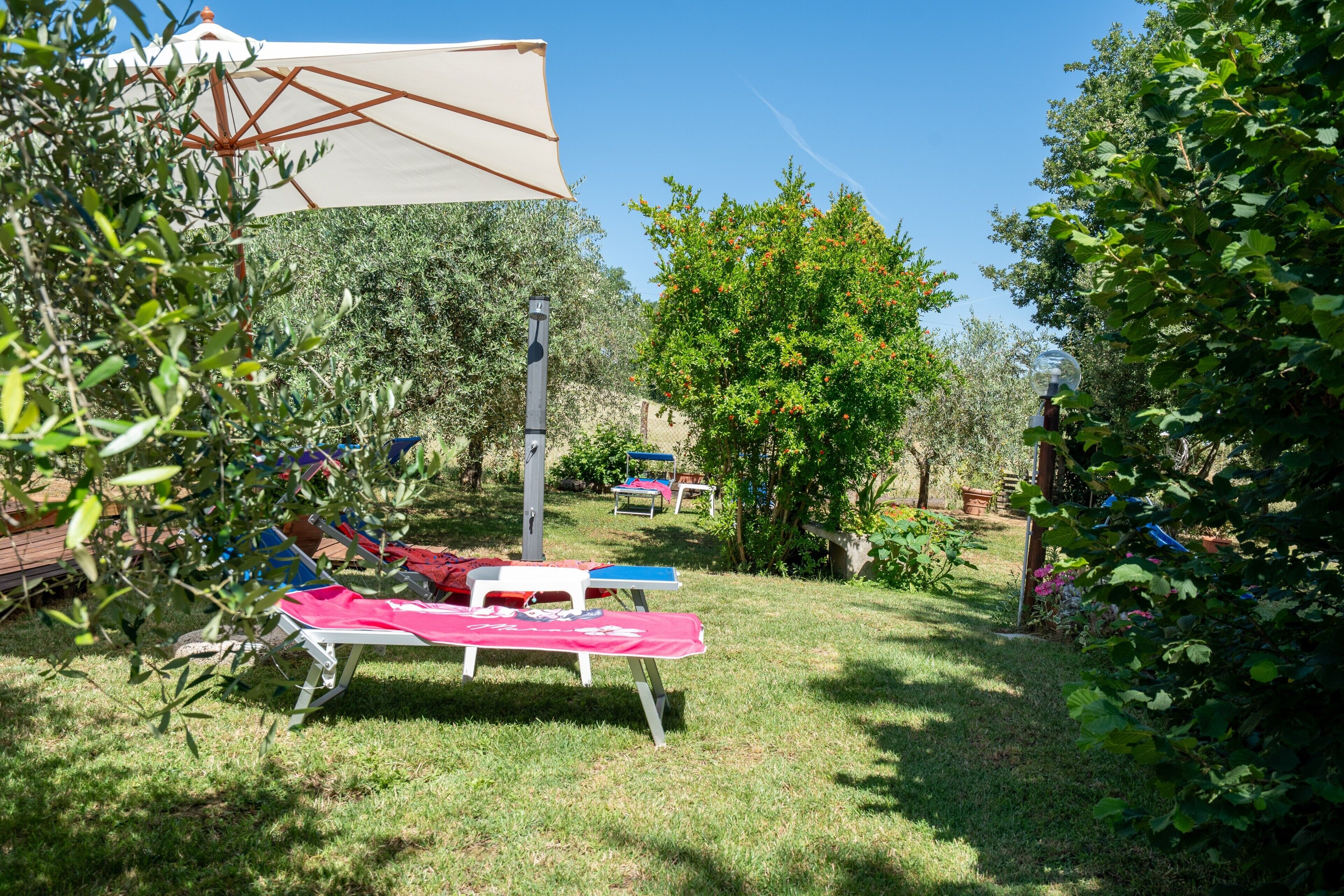 Un'area all'aperto con erba, un ombrellone bianco, una poltrona da relax rossa e bianca e una poltrona da relax blu.