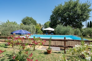 A swimming pool surrounded by a wooden fence, with two umbrellas and potted plants in the foreground.