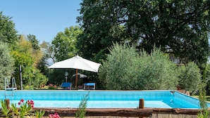 Une piscine dotée d’une terrasse en bois, entourée d’une végétation luxuriante et agrémentée d’un grand parasol.