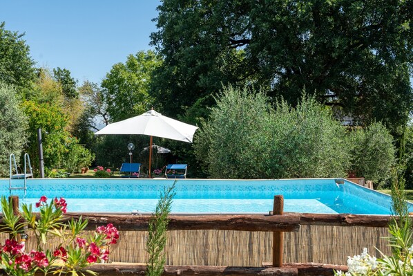 Une piscine dotée d’une terrasse en bois, entourée d’une végétation luxuriante et agrémentée d’un grand parasol.