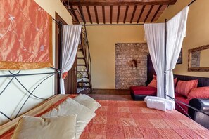 Een slaapkamer met een bed, een stenen muur, een houten ladder, een rode bank en een spiegel.