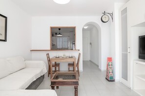 Ein modernes Wohnzimmer mit einer Couch, einem Esstisch aus Holz, einem Couchtisch, einem Fernseher und einer Wanduhr.