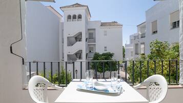A balcony with a white table and chairs, a tray with glasses and a plate, and a view of white buildings with balconies.