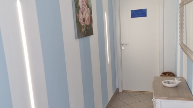 Un pasillo con paredes azul claro, una puerta blanca, un cuadro enmarcado y una pequeña mesa con un cuenco.