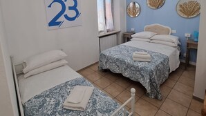 Una habitación con dos camas, una ventana con cortinas, un reloj de pared y un ventilador de techo.