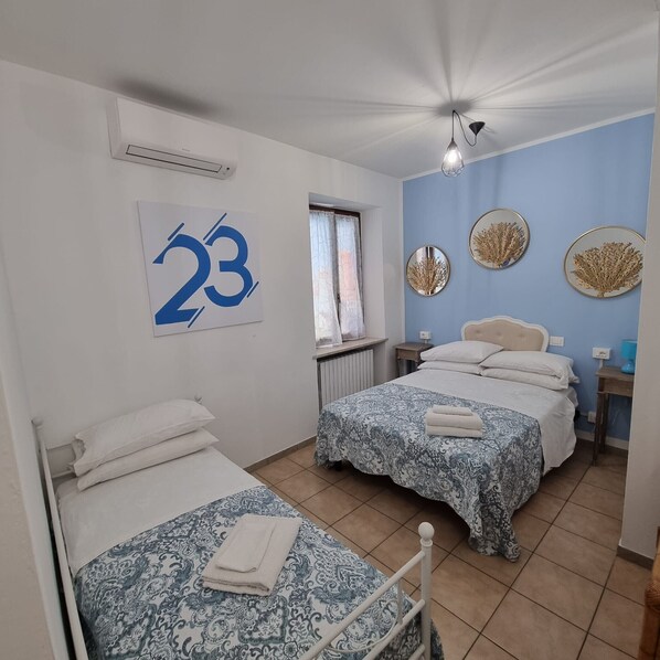 A room with two beds, a window with curtains, a wall clock, and a ceiling fan.
