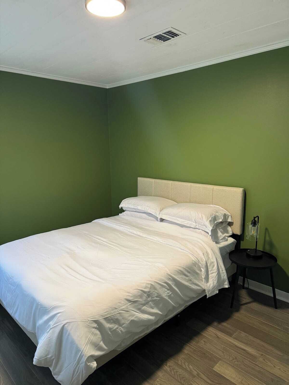 A single bed with white bedding in a room with green walls and a wooden floor.