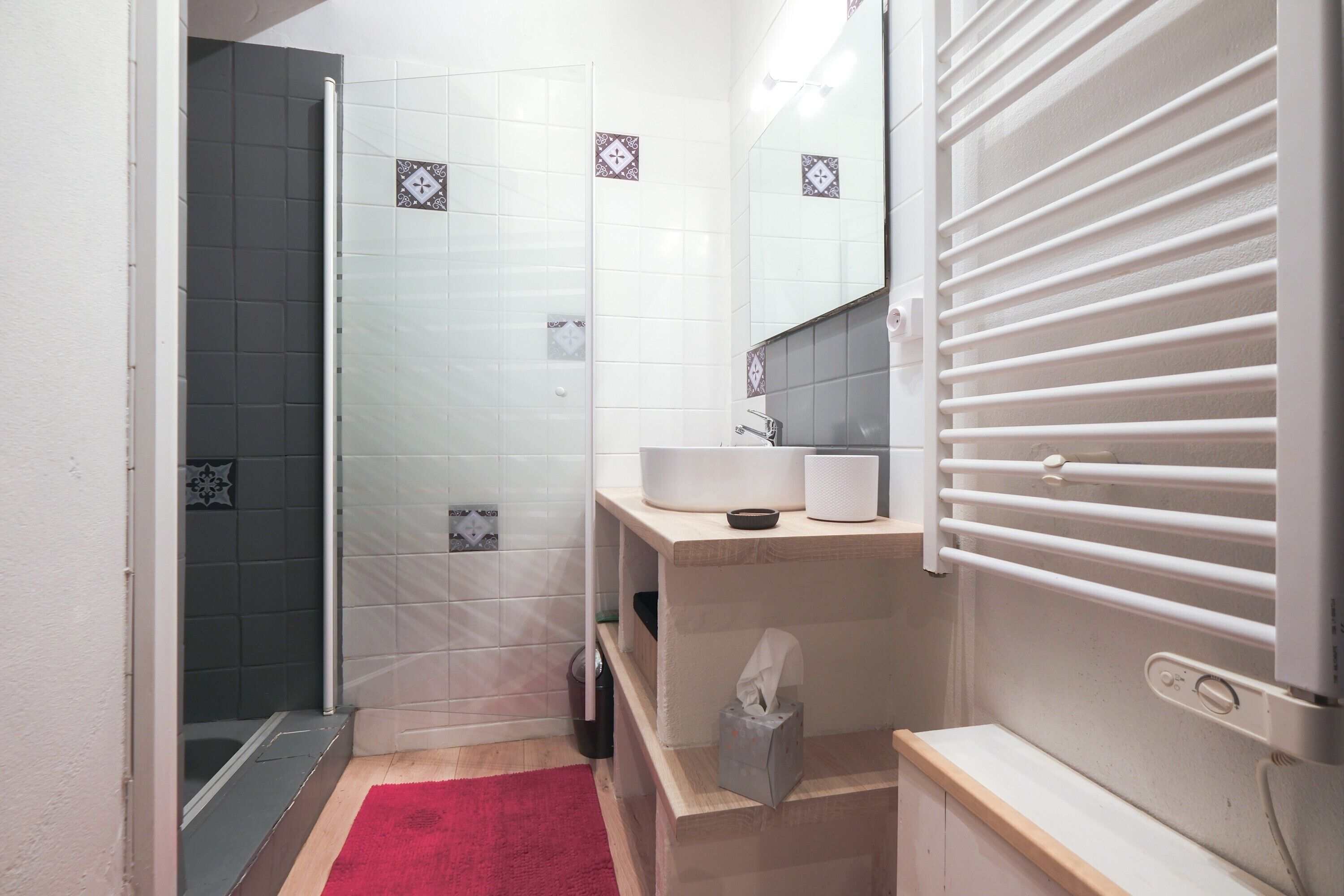 A bathroom with a shower, a sink, a mirror, and a towel dispenser.