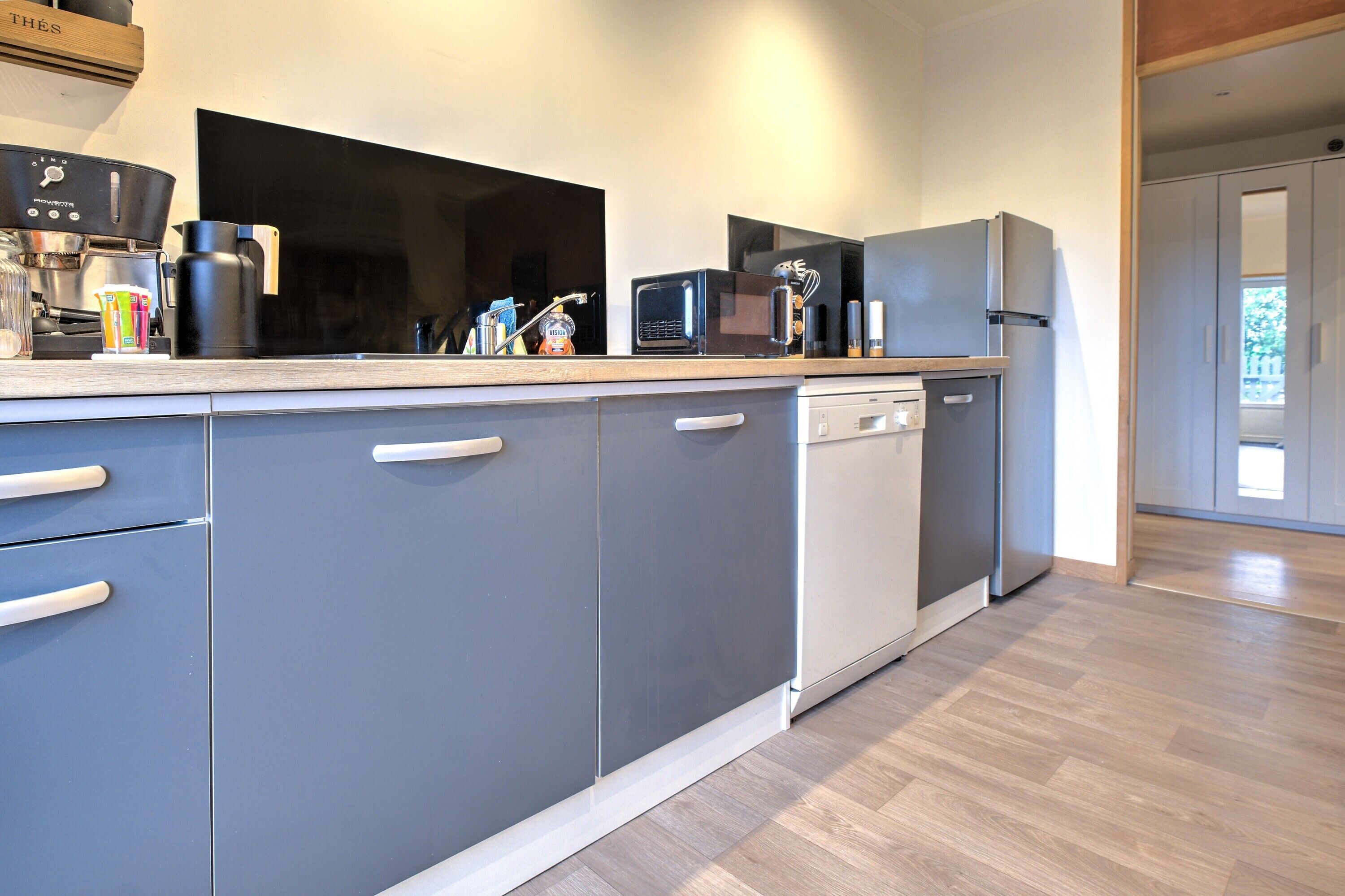 A modern kitchen with grey cabinets, a dishwasher, a coffee maker, and a microwave.
